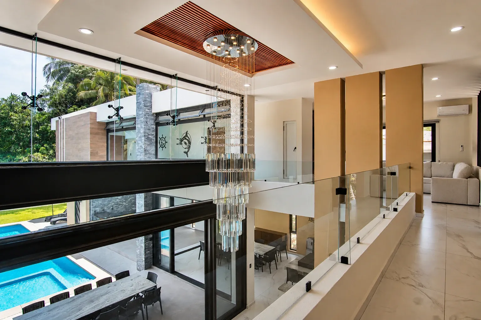 Sala de doble altura con lámpara de cristal y vista a la alberca de la casa de playa