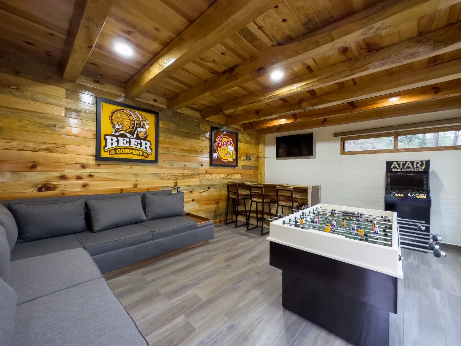 Salón de juegos con futbolito, maquinita arcade y sala, con paredes de madera